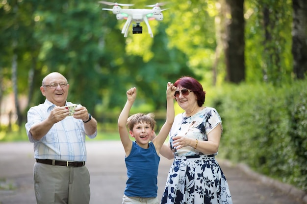 Heureux couple de personnes âgées avec un petit-fils en promenade Un mari, une femme et un enfant âgés lancent un drone