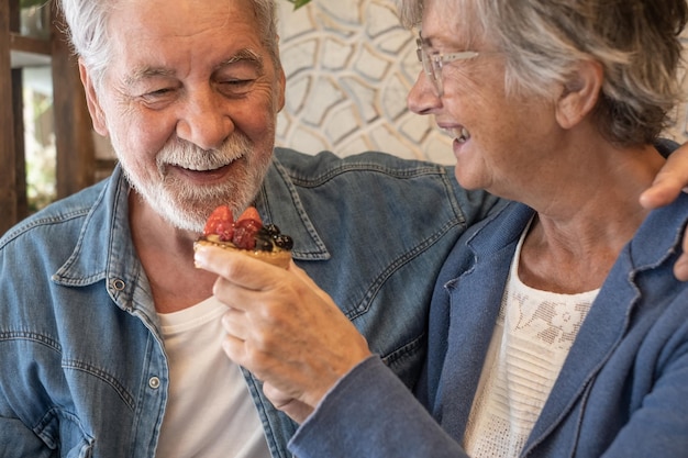 Heureux couple de personnes âgées s'amusant ensemble au café. Femme offrant un petit gâteau aux fruits à son mari