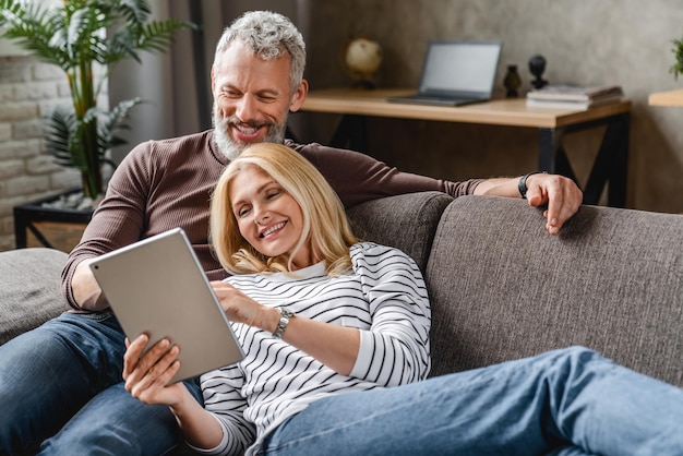 Heureux couple de personnes âgées utilisant une tablette numérique sur un canapé à l'intérieur