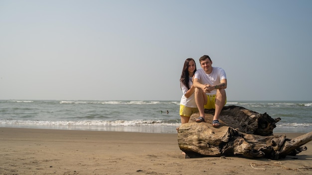 Heureux couple posant sur du bois flotté près de la mer