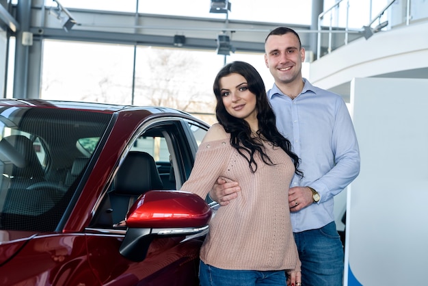 Heureux couple posant avec de nouvelles voitures dans la salle d'exposition