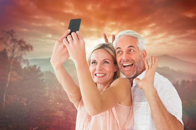 Heureux couple posant pour un selfie contre le lever du soleil sur les montagnes