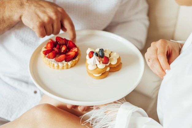 Heureux couple prenant son petit déjeuner au lit avec de délicieux biscuits aux fraises sur le dessus