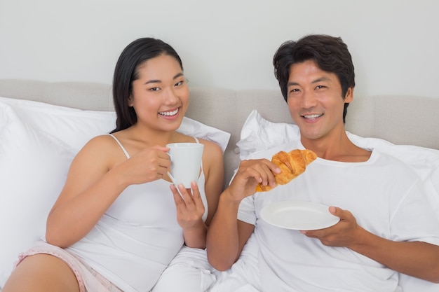 Heureux couple prenant son petit déjeuner au lit