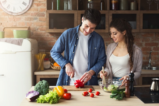 Heureux couple préparant le dîner ensemble dans leur cuisine loft à la maison. Faire une salade de légumes.