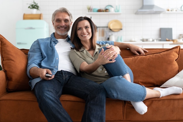 Heureux couple regardant un film à la télévision assis sur un canapé à la maison.