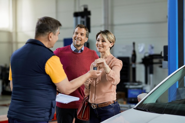 Heureux couple remettant les clés de voiture à leur réparateur automobile dans un atelier