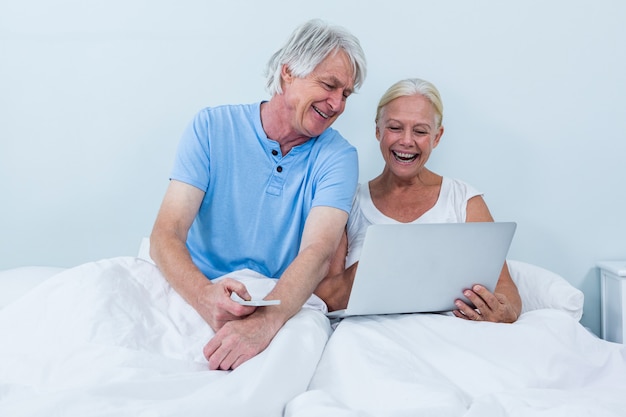 Heureux couple de retraités à l'aide d'un ordinateur portable assis sur le lit