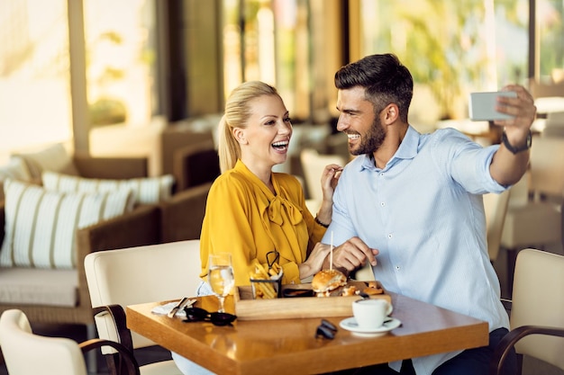 Heureux couple s'amusant tout en prenant selfie pendant le déjeuner dans un restaurant