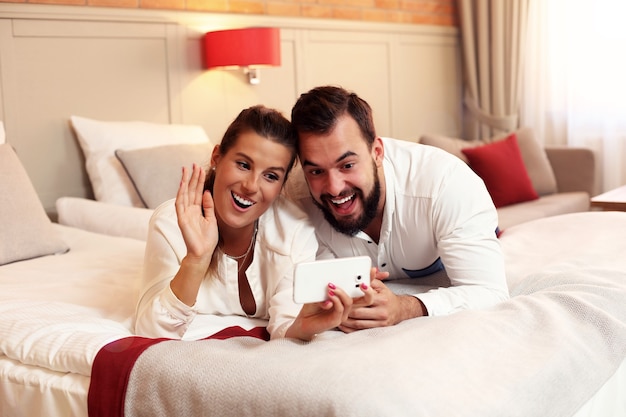 Heureux couple se reposant dans une chambre d'hôtel et utilisant un smartphone