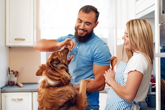 Heureux couple souriant, cuisiner des aliments à la cuisine avec leur chien