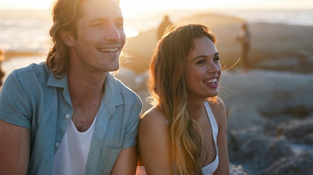 Heureux couple souriant sur la plage au coucher du soleil profitant de l'été