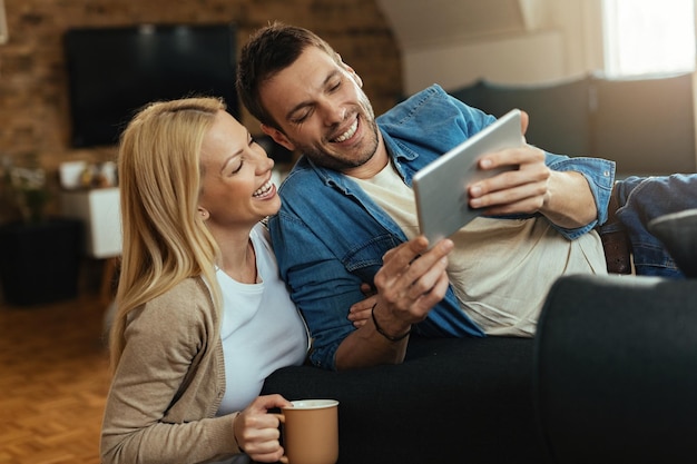 Heureux couple surfant sur le net sur le pavé tactile tout en se relaxant dans le salon