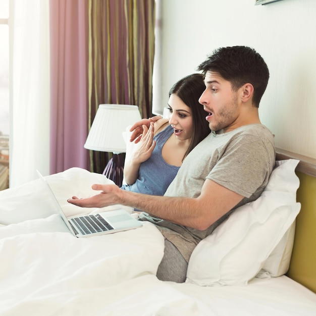 Heureux couple surpris en regardant un film sur un ordinateur portable au lit le matin