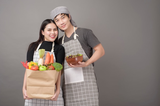 Heureux couple tient des légumes dans un sac d'épicerie mur gris