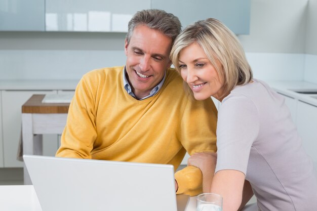 Heureux couple utilisant un ordinateur portable dans la cuisine