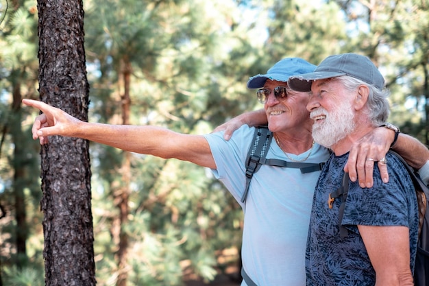 Heureux couple de vieux hommes actifs avec chapeau et sac à dos embrasser et s'amuser en randonnée en montagne dans les bois en appréciant l'aventure et la liberté des personnes âgées à la retraite et le concept de mode de vie sain