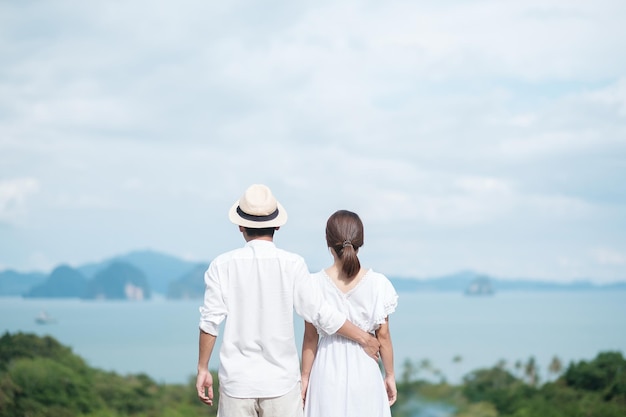 Heureux couple voyageur en chemise blanche et robe profiter Belle vue Les touristes debout et se détendre sur l'océan voyagent ensemble aiment le concept d'été et de vacances