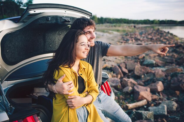 Heureux couple de voyageurs assis dans le coffre ouvert de la voiture et regarder le lever du soleil.