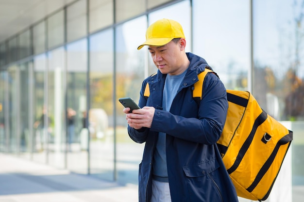 Heureux coursier masculin marchant fournisseur de nourriture, dans l'attente d'une nouvelle commande reçue dans l'application téléphonique, courrier asiatique