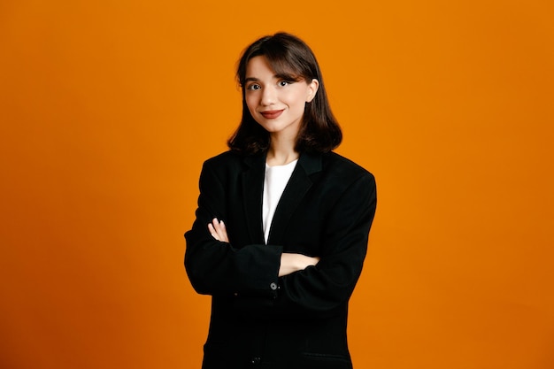 Heureux croisant les mains jeune belle femme portant une veste noire isolée sur fond orange