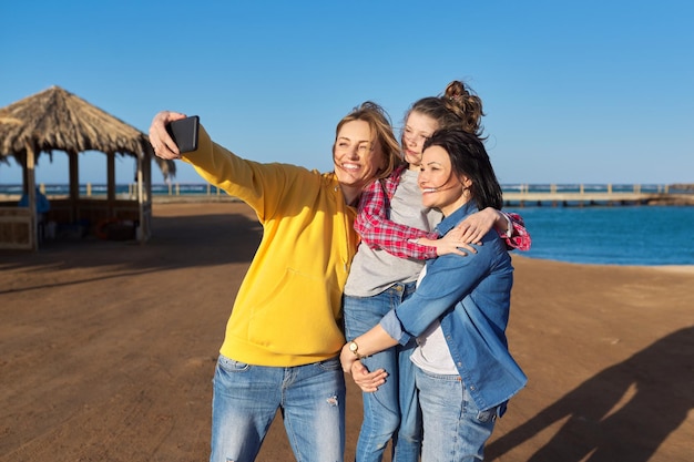 Heureux deux femmes d'âge moyen et une petite fille prenant selfie sur fond de plage mer smartphone