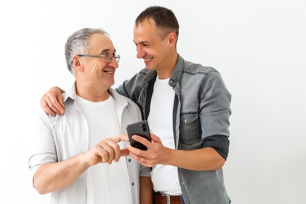 Heureux deux générations d'hommes de la famille vieux père embrassant un jeune fils adulte s'amusant à utiliser un téléphone intelligent en regardant une vidéo amusante sur les réseaux sociaux à l'aide d'applications mobiles