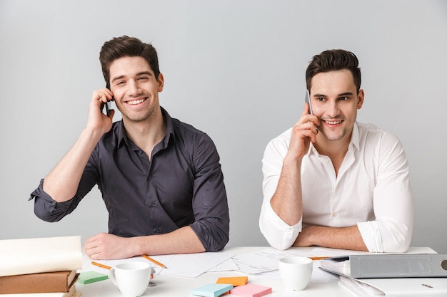 Heureux deux jeunes hommes d'affaires parlant par téléphones mobiles.