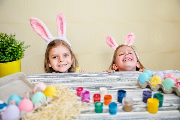 Heureux deux petites filles dans des oreilles de lapin, jetant un coup d'œil derrière la table avec des oeufs de pâques colorés