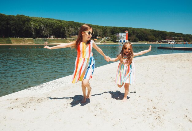 Heureux deux petites filles s'amusent et courent joyeusement sur la plage sautent sur le sable