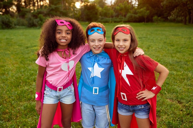 Heureux divers enfants de super-héros étreignant dans le parc d'été