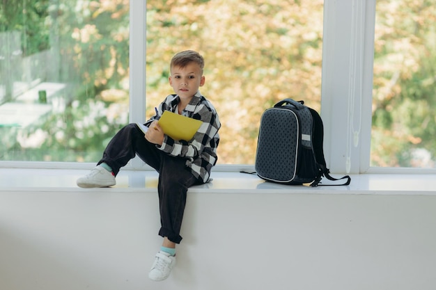 Heureux écolier dans des vêtements décontractés avec des sacs à dos souriant et lisant des notes dans des cahiers tout en faisant ses devoirs à la maison