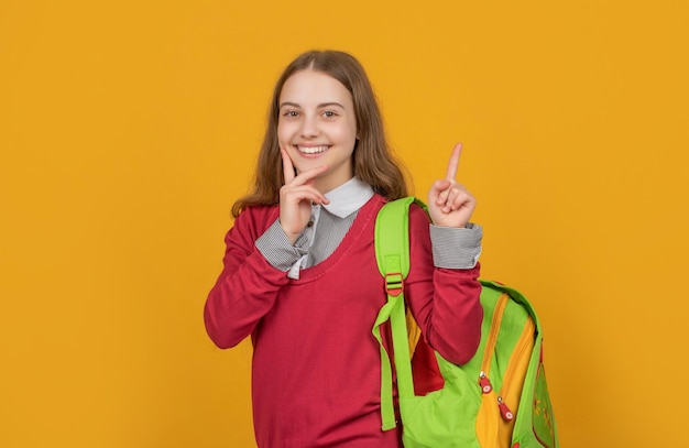 Heureux écolier gardant le doigt levé portant l'idée de fond jaune sac d'école