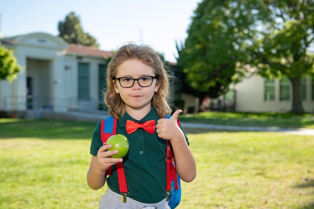 Heureux écolier souriant élève dans des verres avec le pouce vers le haut va à l'école pour la première fois Enfant avec sac d'école Enfant à l'extérieur de l'école