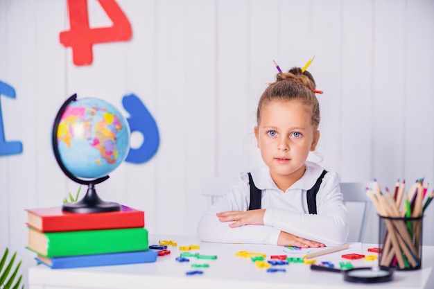 Heureux élève souriant au bureau. Enfant dans la salle de classe avec des crayons, des livres. Kid fille de l'école primaire.