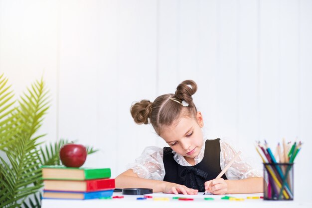 Heureux élève souriant au bureau. Fille dans la salle de classe avec des crayons, des livres. Kid fille de l'école primaire.