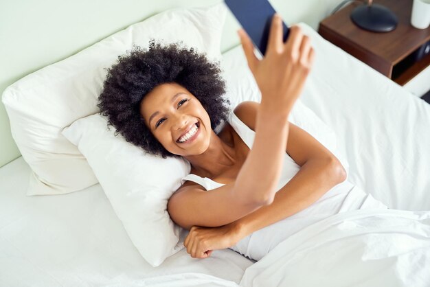 Heureux d'embrasser un autre jour alors je prends un selfie Photo recadrée d'une jolie jeune femme prenant un selfie au lit à la maison