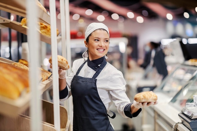 Heureux employé du département de pâtisserie tenant des petits pains et souriant à un client au supermarché