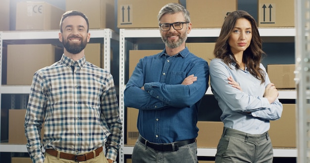 Heureux employés de poste masculins et féminins souriants debout dans le magasin de courrier, croisant les mains devant et souriant joyeusement