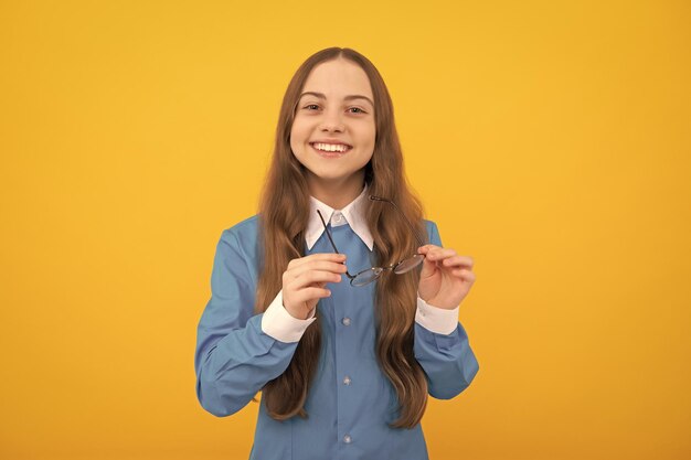 Heureux enfant d'âge scolaire tenir des lunettes pour la correction de la vision fond jaune