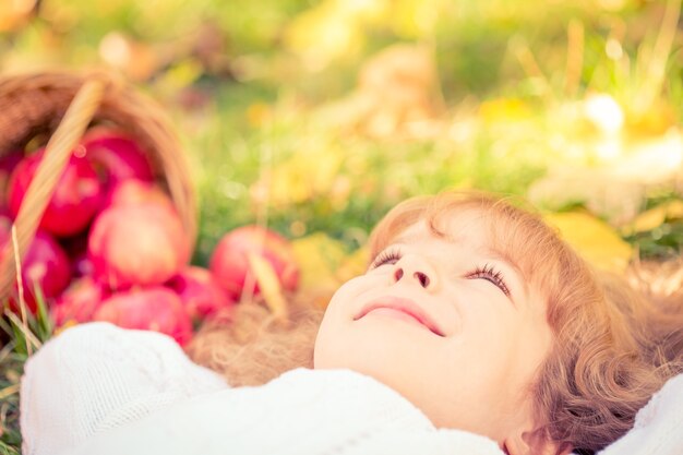 Photo heureux enfant allongé sur les feuilles d'automne. enfant drôle dehors en parc d'automne