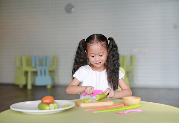 Heureux enfant asiatique fille trancher le concombre sur une planche à découper