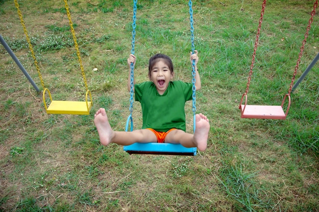 Heureux enfant asiatique jouer balançoire aire de jeux extérieure