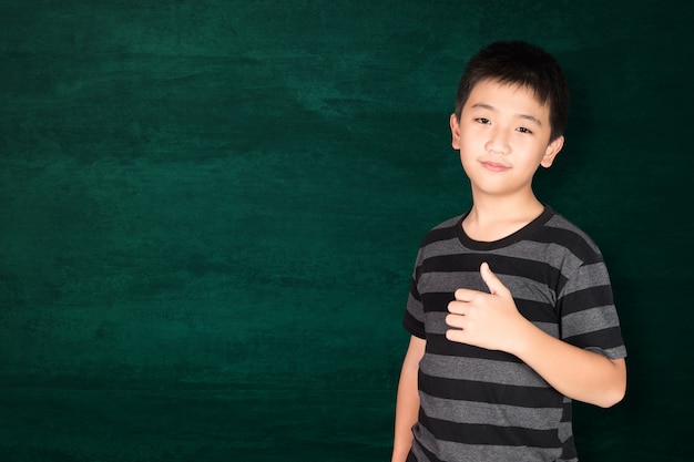 Heureux enfant asiatique souriant sur un tableau vert vide