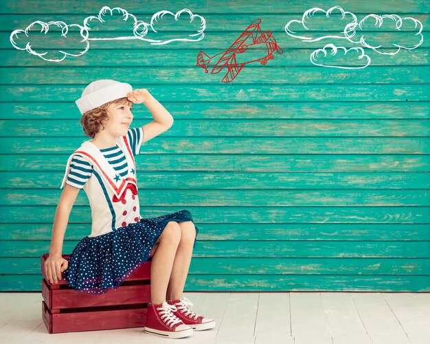 Heureux enfant assis sur une vieille valise habillé comme un marin à l'avenir sur fond de bois bleu