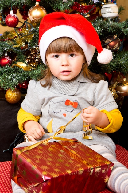 Heureux enfant au bonnet de Noel ouvrant la boîte de cadeau de Noël