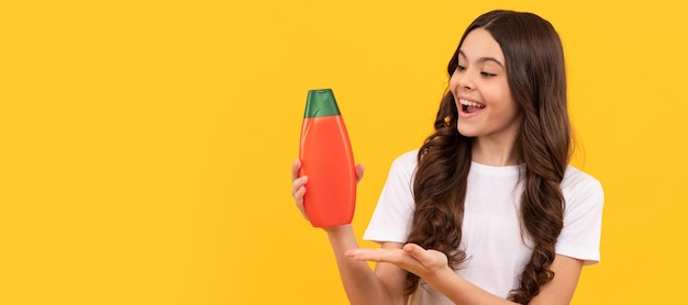 Heureux enfant aux cheveux longs présentant le produit de la proposition de produit de bouteille de shampooing Bannière d'en-tête d'affiche de studio de soins capillaires enfant fille avec espace de copie