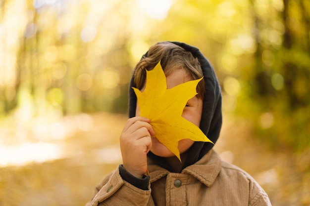 Heureux enfant bébé garçon riant et jouant dans la journée d'automne, l'enfant se couvre le visage de feuilles