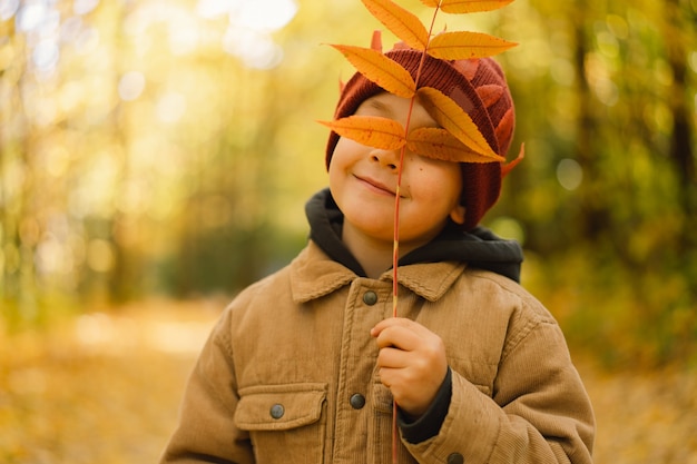 Heureux enfant bébé garçon riant et jouant dans la journée d'automne, l'enfant se couvre le visage de feuilles