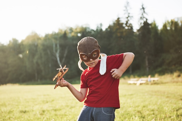 Heureux enfant en casque pilote jouant avec un avion jouet en bois et rêvant de devenir volant